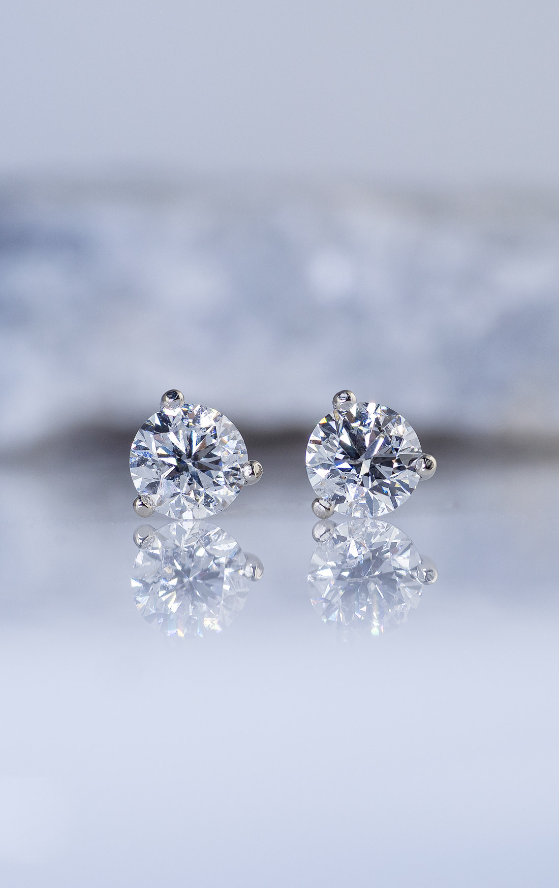 A pair of diamond stud earrings in 14k white gold martini settings in front of a rock on a light background