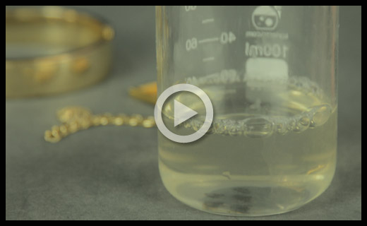A beaker filled with a clear solution next to gold jewelry