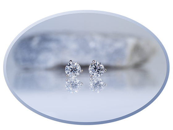 A pair of diamond stud earrings on a light background in front of a rock