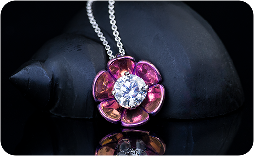A magenta lotus flower pendant with a lab diamond center in front of a black shell