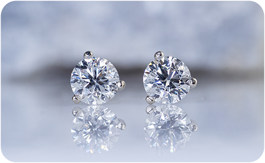 A pair of diamond stud earrings on a light background in front of a rock