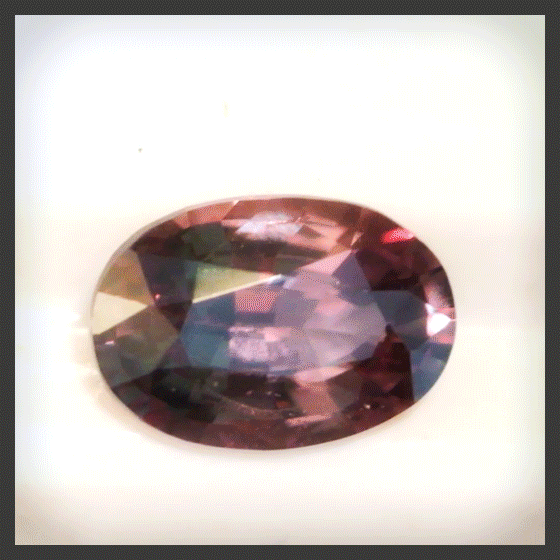 An oval alexandrite gemstone that shifts in color under different lights from red to green and back