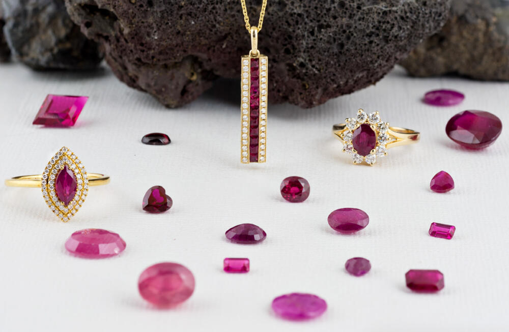 A group of loose rubies alongside two rings and a pendant set with rubies
