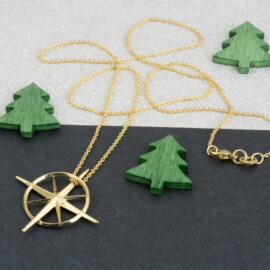 yellow gold true north necklace laying flat on fancy background