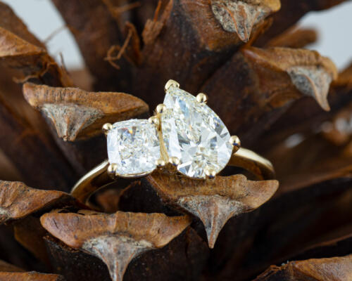 Two stone ring with pear and cushion cut lab diamond on yellow gold setting in pine cone