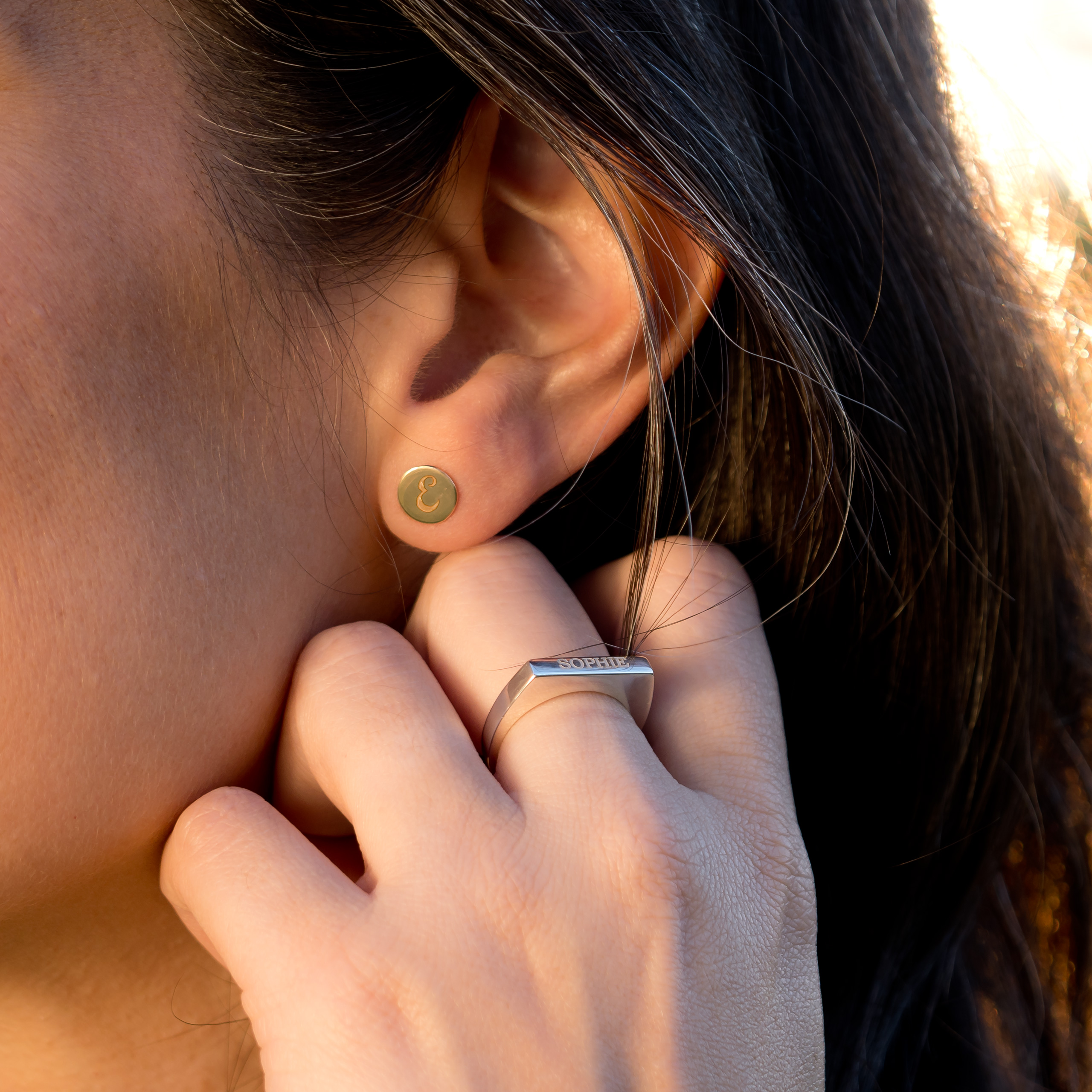 An engraved circular earring with the letter E and a ring engraved with the name Sophie being worn