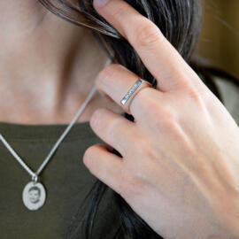 Engravable stacking ring being worn with oval pendant in background