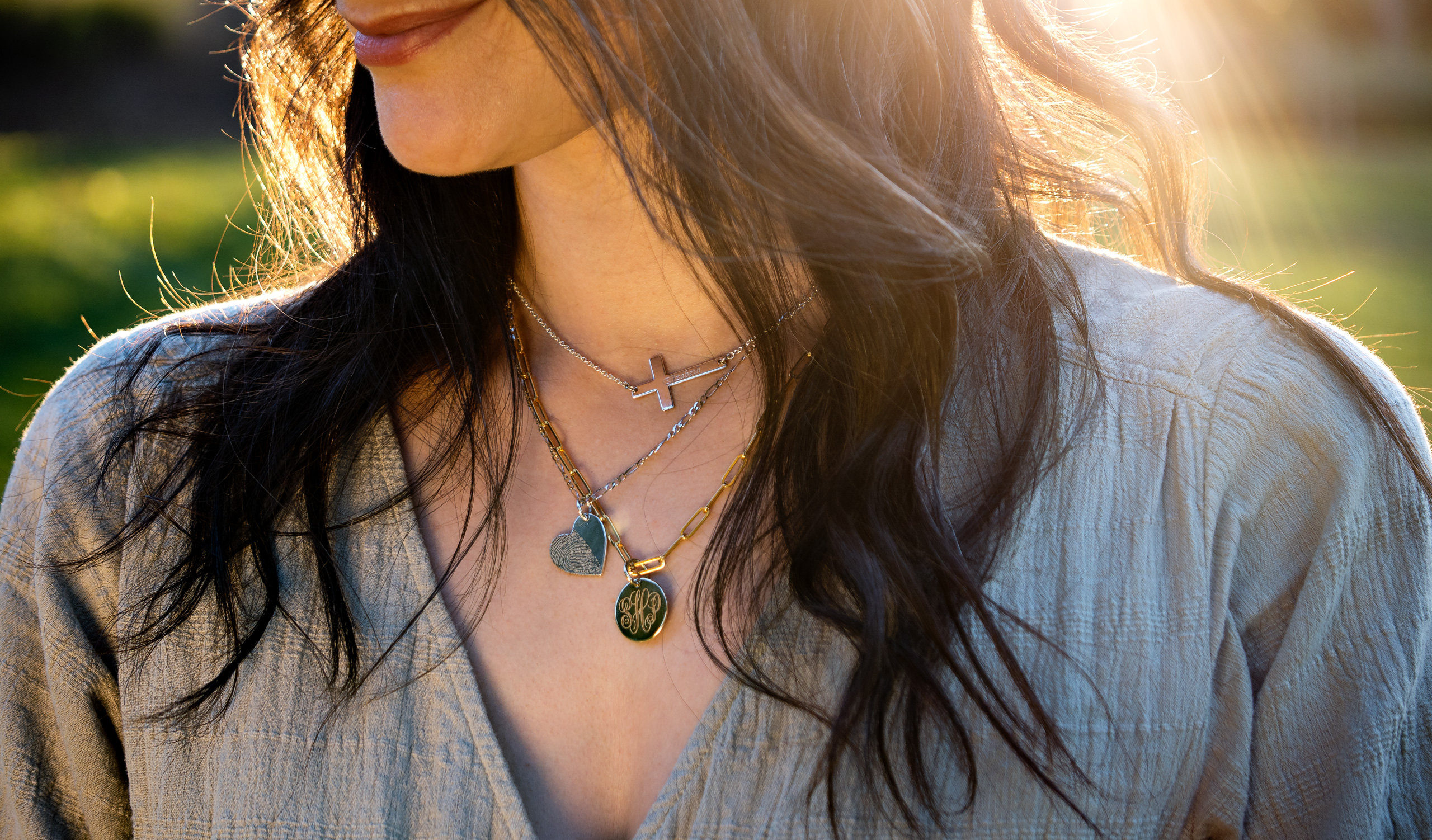 Three engraved necklaces a cross a heart and a disc being worn at sunset