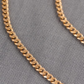 A close up of a rose gold curb chain
