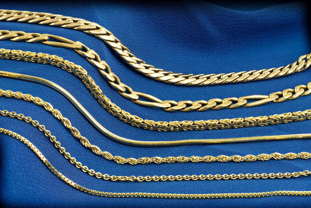 A group of yellow gold chains of different kinds of a blue background