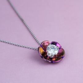 Lotus blossom pendant with magenta titanium and round lab diamond on 14k white gold chain in laying on pink background