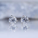 A pair of diamond stud earrings in 14k white gold martini settings in front of a rock on a light background