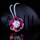 A bright pink lotus flower pendant on a white gold chain resting on a black shell with the word Titanium placed subtly in the background