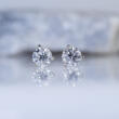 A pair of diamond stud earrings in 14k white gold martini settings in front of a rock on a light background